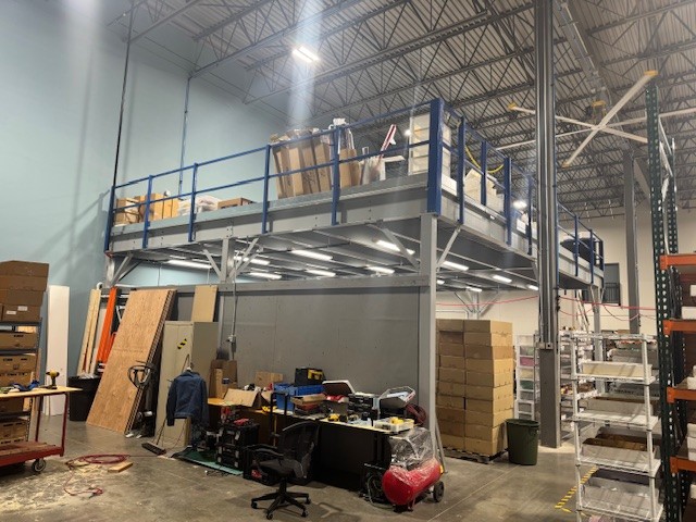 Commercial grade bay door, emergency lighting, and electrical service entrance beneath mezzanine